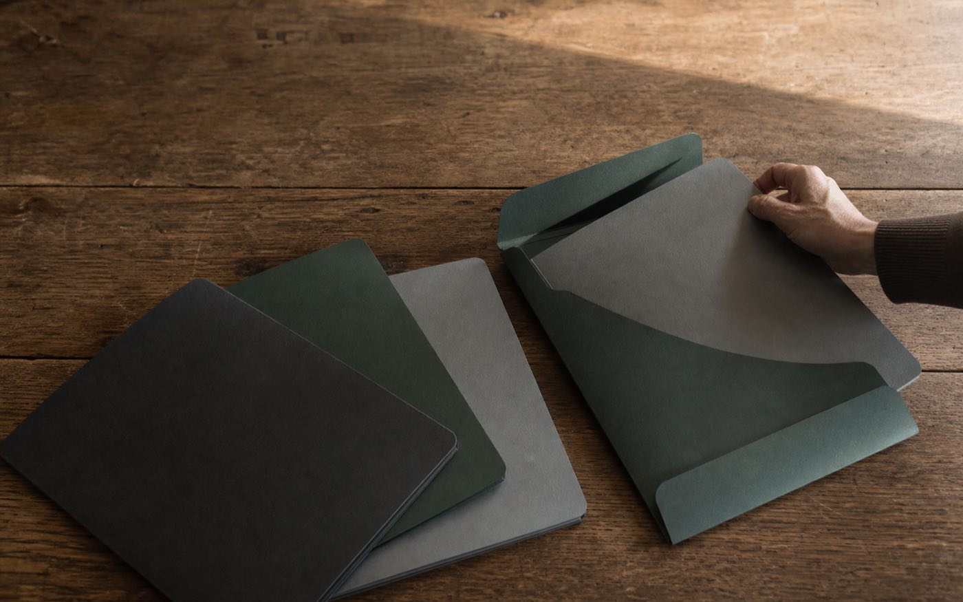 Several unmarked folders being brought together on a wood surface
